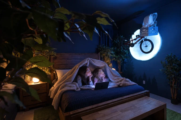 Sisters share a tablet in a blanket fort under the glowing moon in The Extra-TerRestful Suite at Electronic Ice Castle