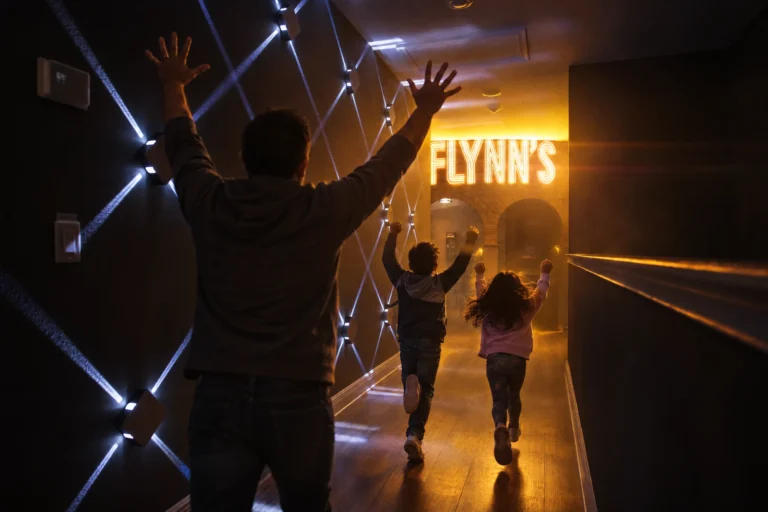 A dad cheers as his kids run down the glowing hallway into Flynn's Arcade at Electronic Ice Castle