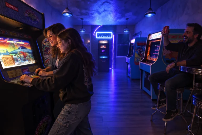 A mom and daughter play a retro arcade game as dad cheers from the bar in Flynn's Arcade at Electronic Ice Castle