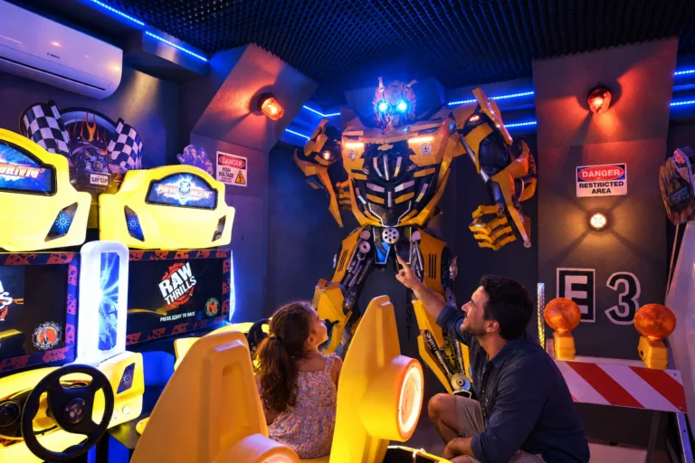 A little girl meets the 10-foot robot beside the racing seats in the Robot Game Room at Electronic Ice Castle