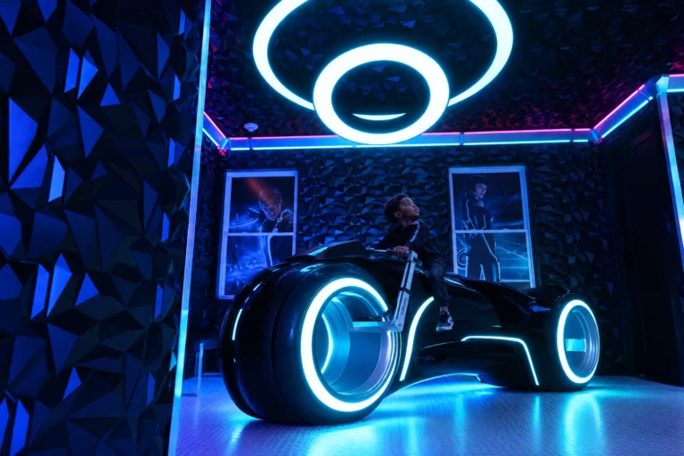 A boy sits on the glowing neon motorcycle under the light rings of The Grid "The Secret Suite" at Electronic Ice Castle