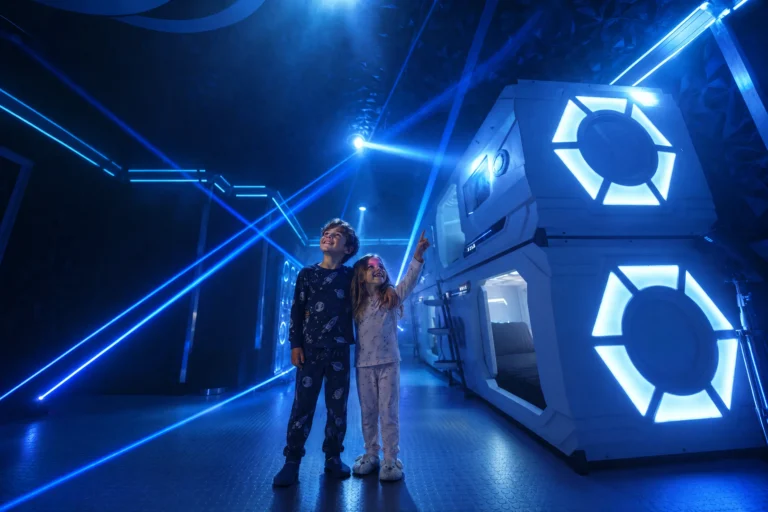 Two kids in pajamas look up at the lasers in the corridor of The Grid "The Secret Suite" at Electronic Ice Castle