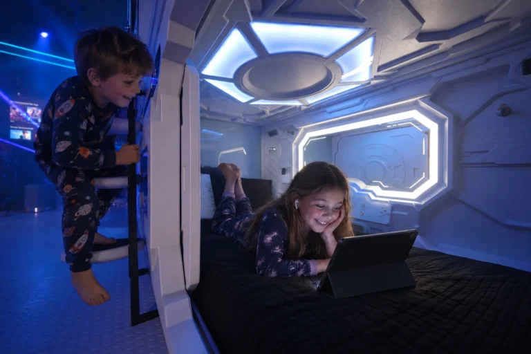 A girl watches her tablet in her sleeping pod while her brother climbs the ladder in The Grid "The Secret Suite" at Electronic Ice Castle