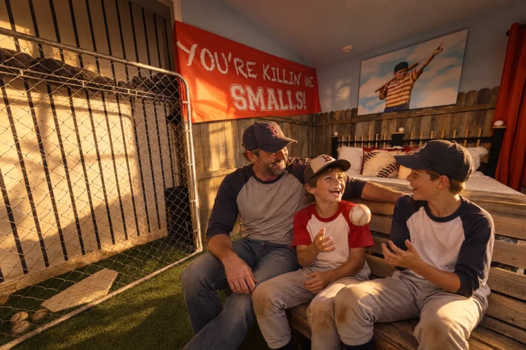 A dad and his boys sit on the bleachers in The Slumber Lot baseball bedroom at Electronic Ice Castle