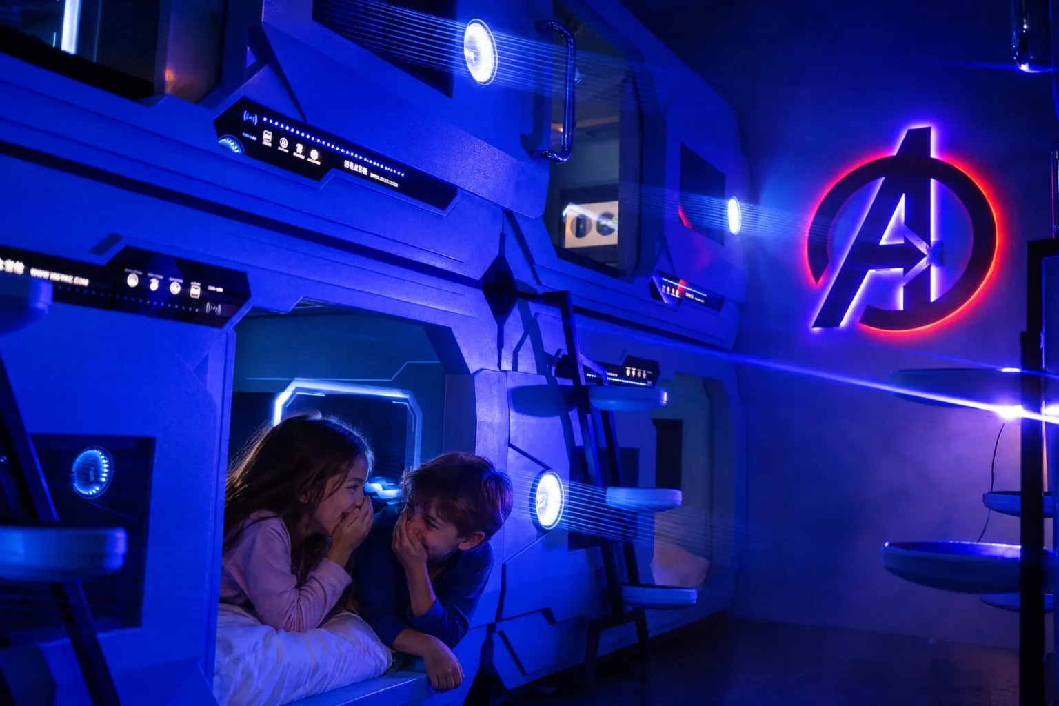 Two kids whisper and giggle in their glowing bunk pod in the Stark Tactical Recovery Wing at The Iron Mansion